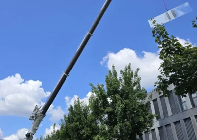 Kran hebt eine Glasscheibe für die Reparaturverglasung an einem modernen Gebäude.