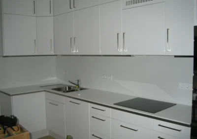 Weiße Küchenzeile mit passgenauer Glasrückwand hinter Spüle und Kochfeld.